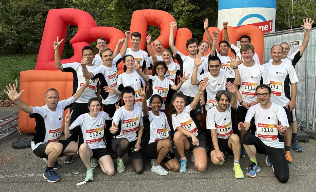 A group of cheering Q.ANT employees in running clothing in front of the B2Run logo sign