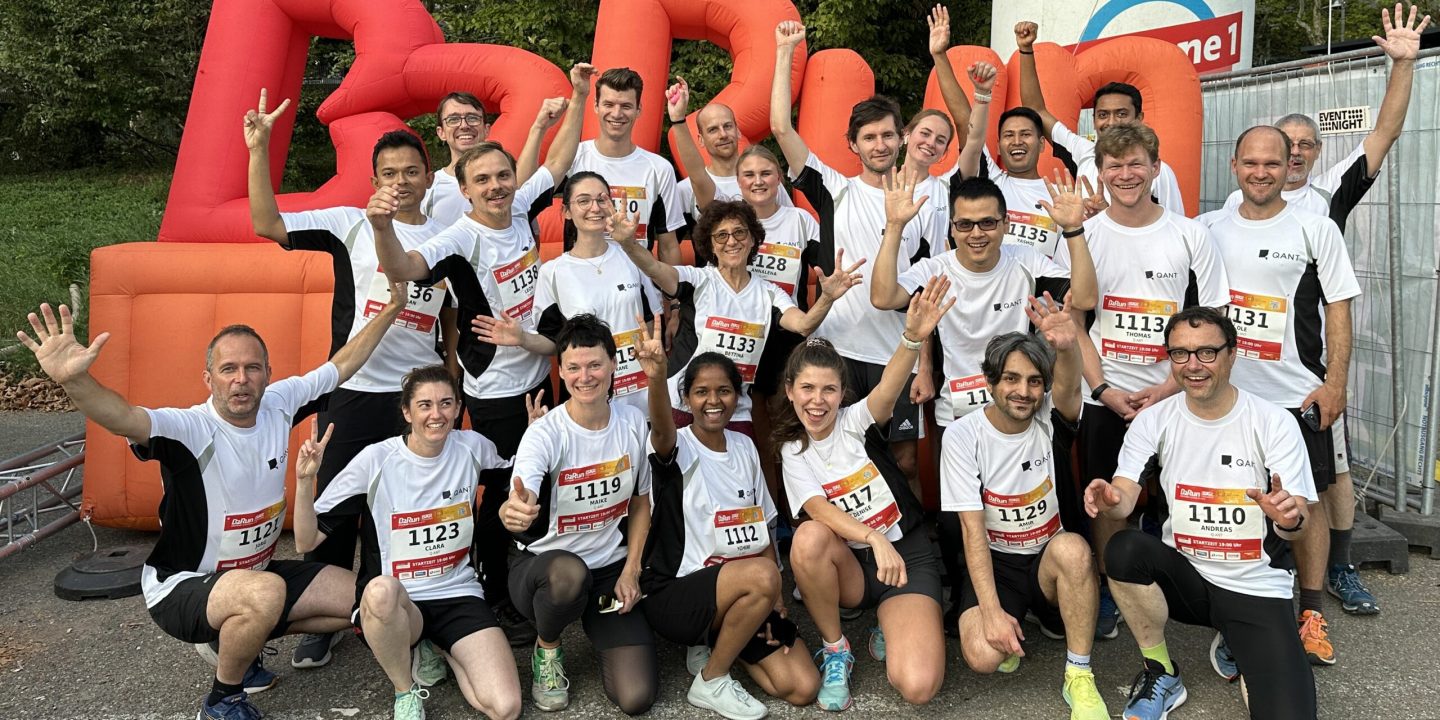 A group of cheering Q.ANT employees in running clothing in front of the B2Run logo sign
